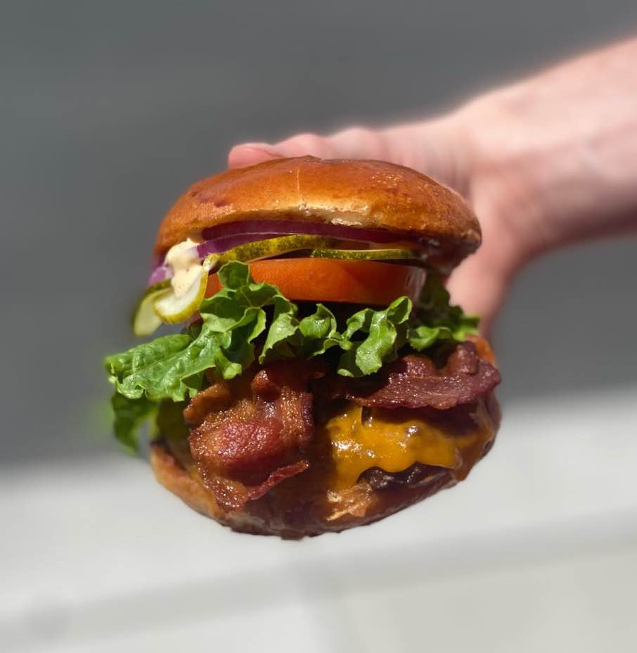 Hand holding a bacon cheeseburger